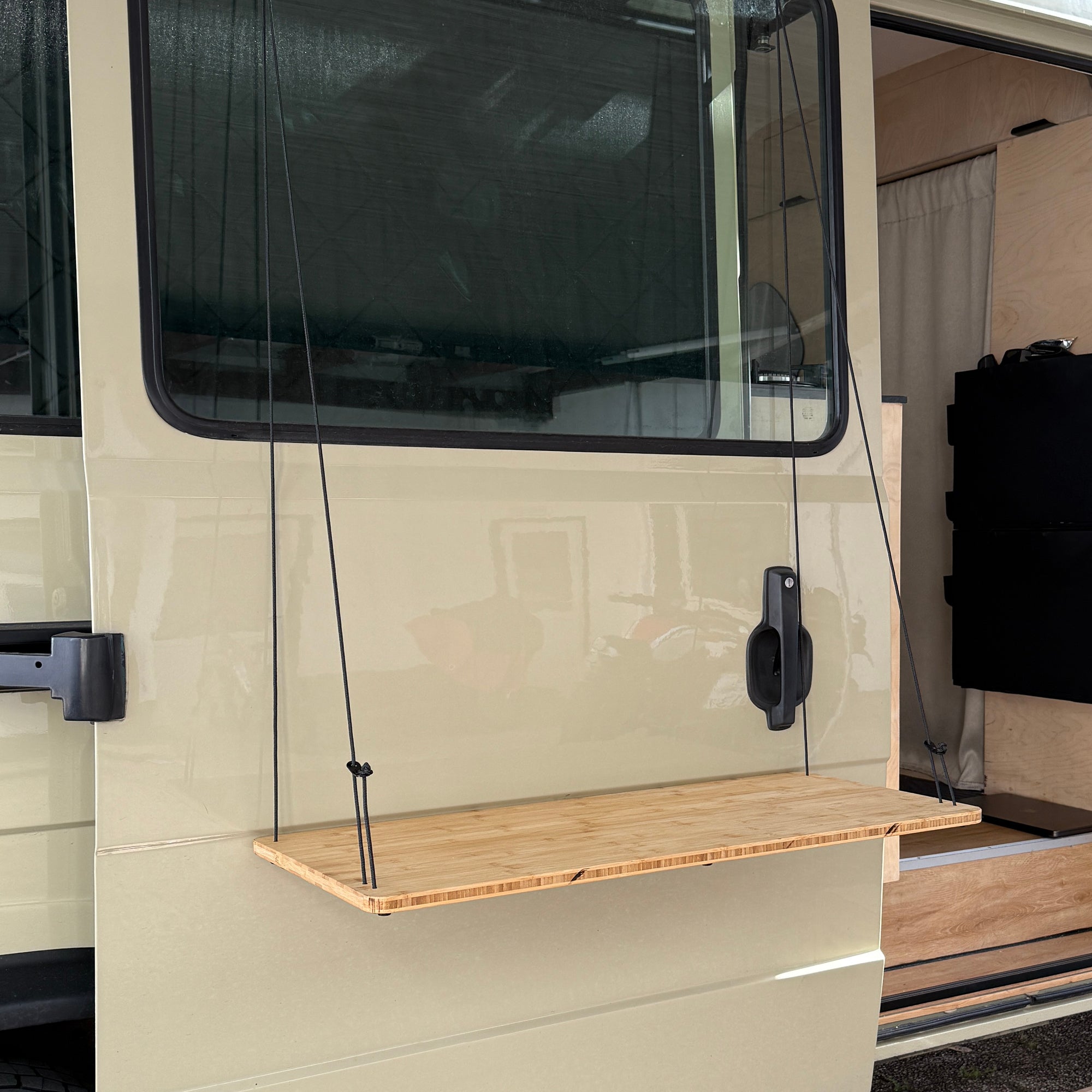 Klappen-Werktisch aus Holz ist an der Seite eines Vans befestigt, mit stabilen Seilen zur Unterstützung.